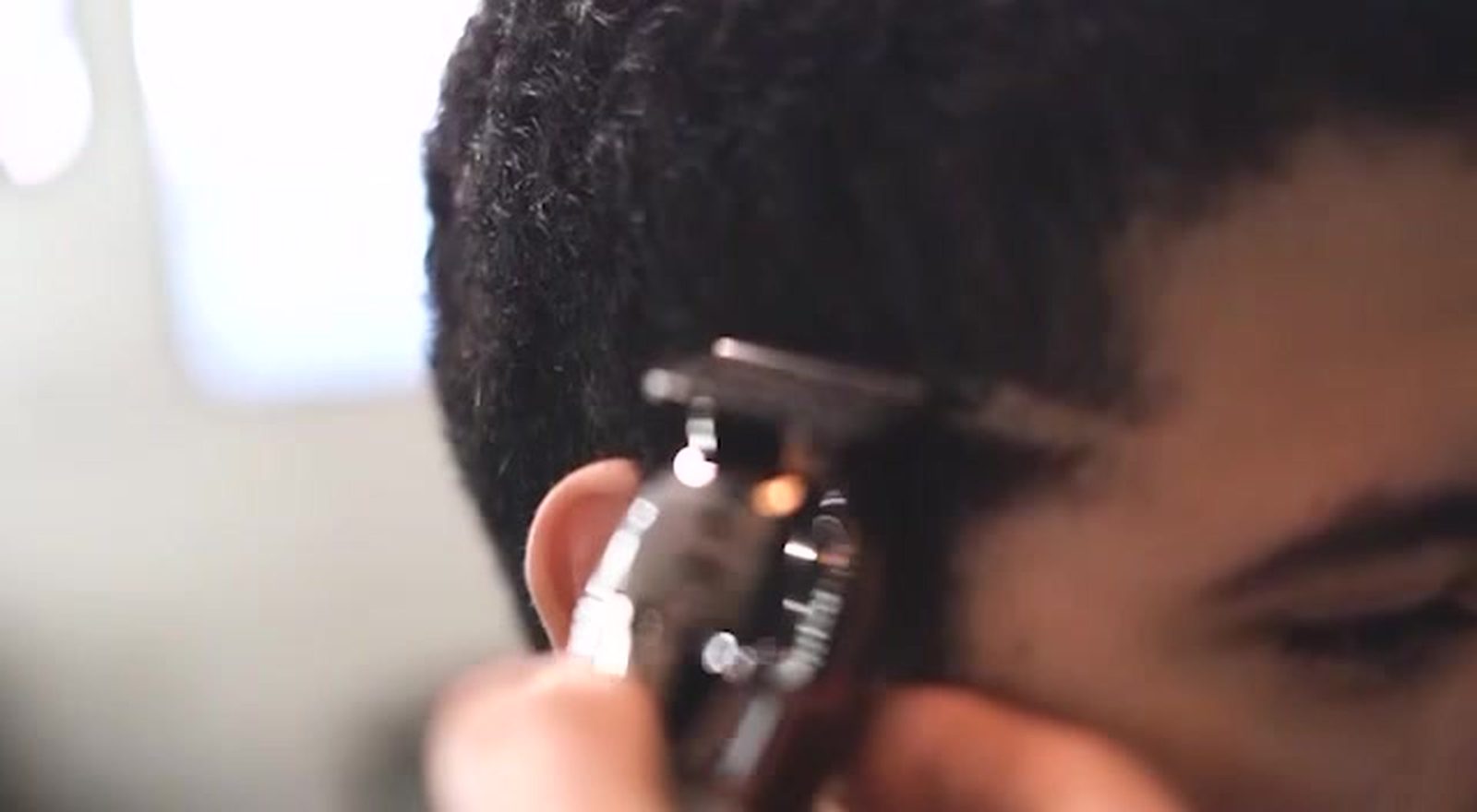 Clippers working a fade at the temple in close detail, the barber's hand steadying the client's head.