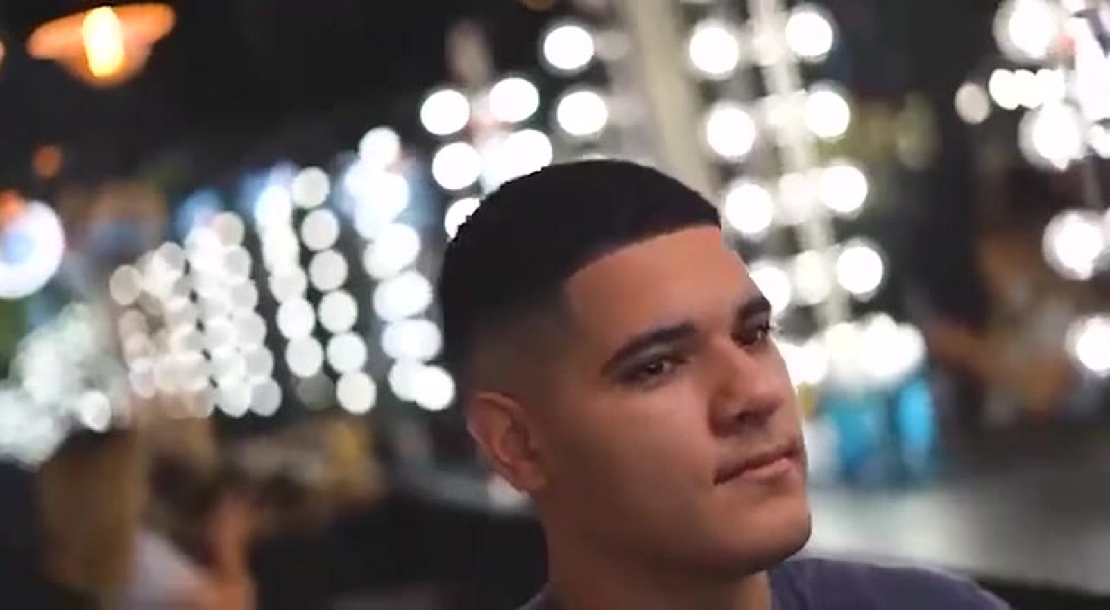 Three-quarter portrait of a client with a fresh fade, warm mirror lights out of focus behind him.